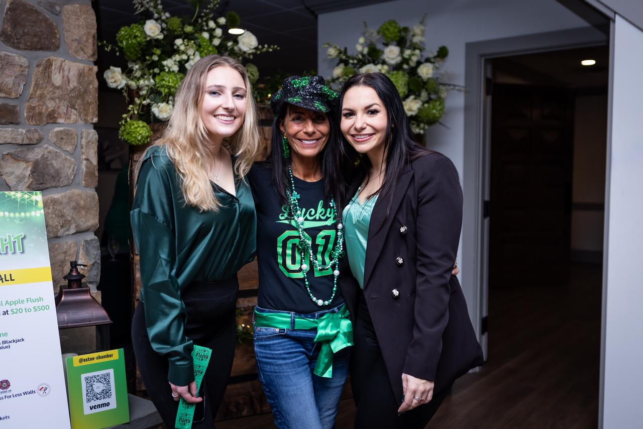 Three women posing together at an event, with one donning st. patrick's day-themed attire.