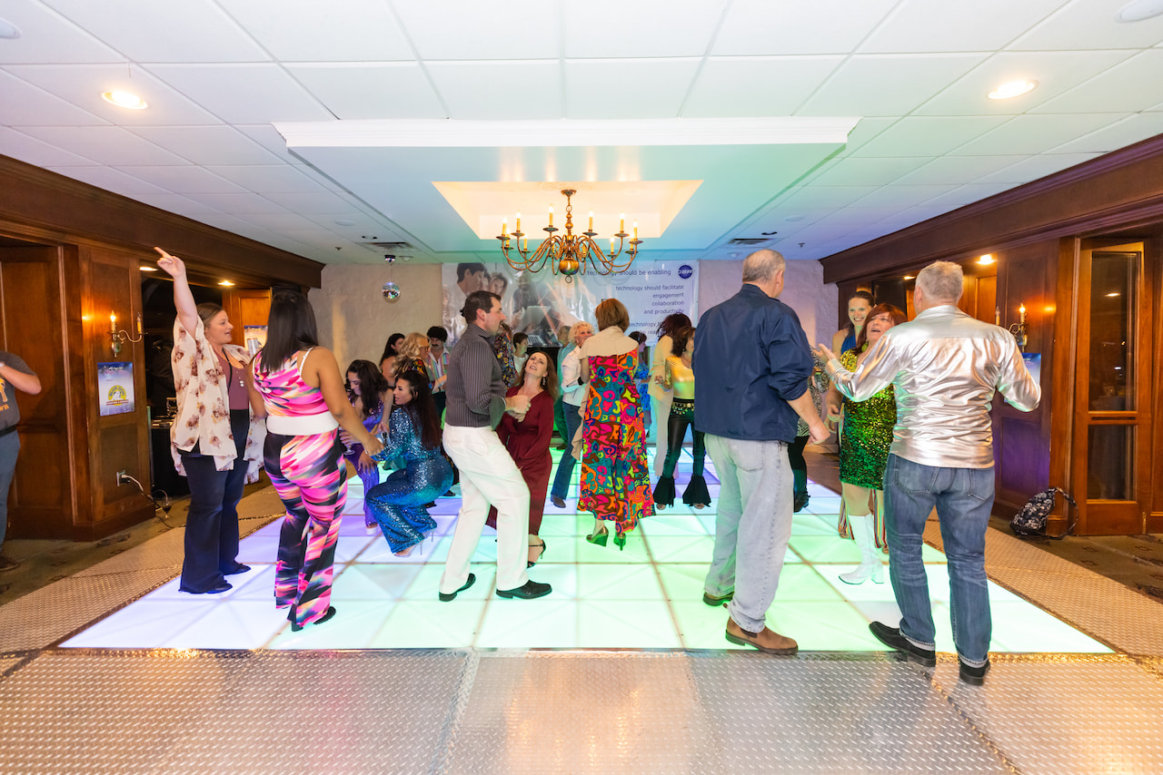Group of people dancing and socializing on a lit dance floor at an indoor event.