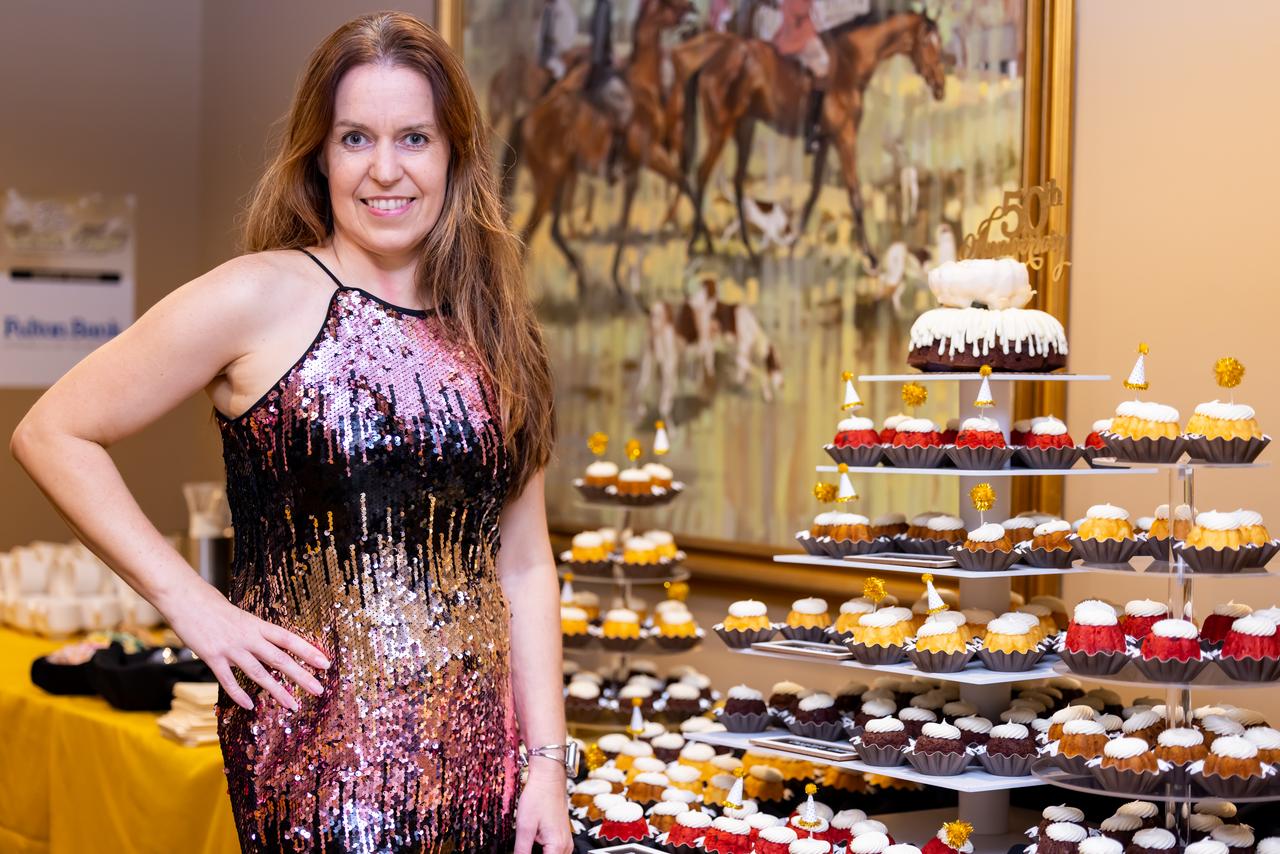 A woman in a sequined dress standing next to a display of cupcakes at an event.