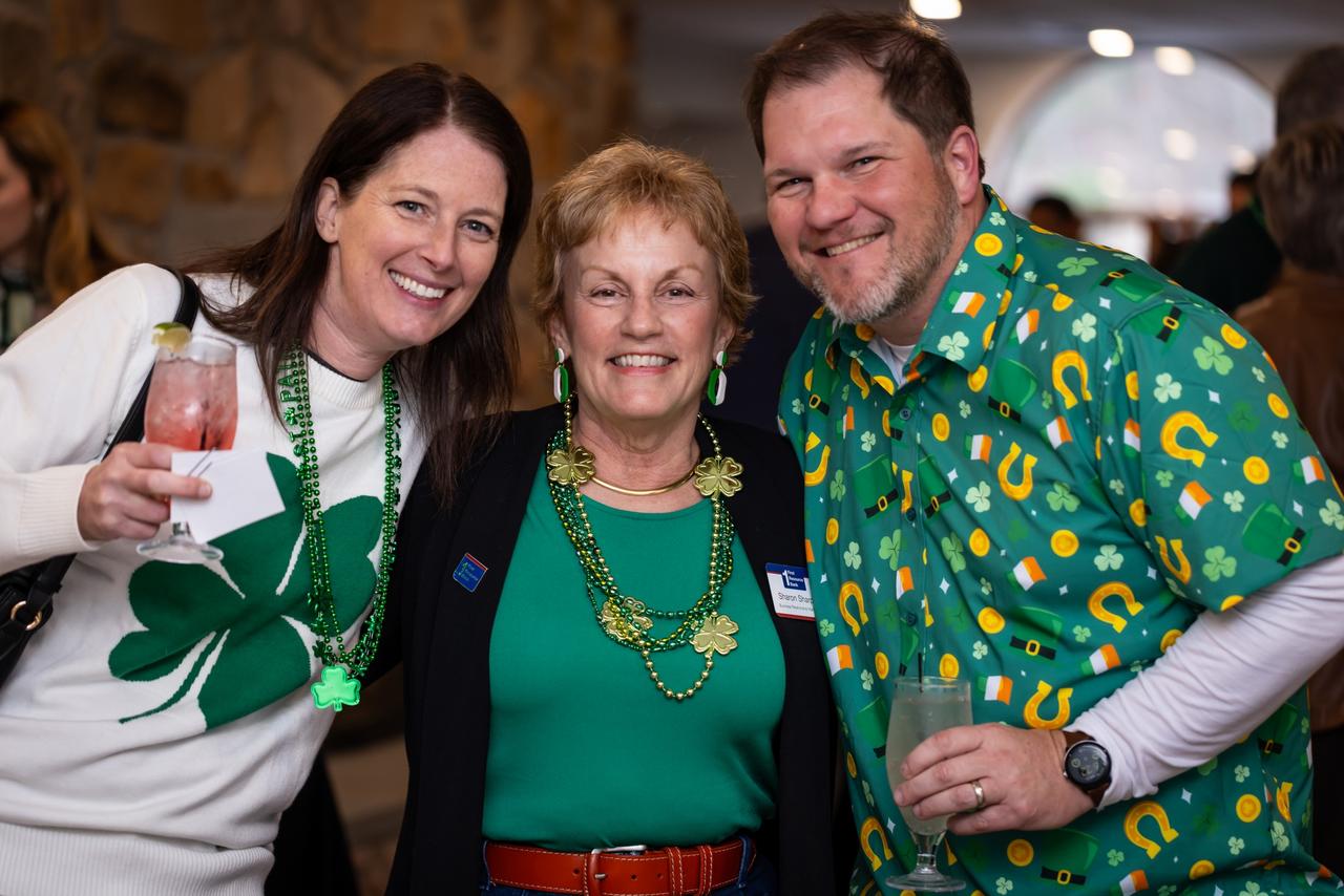 Three people celebrating, possibly at a st. patrick's day event, with one person wearing a shirt with shamrock patterns.